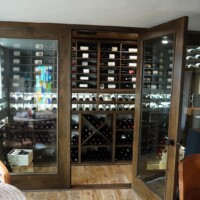 An LVL (laminated veneer lumber) core door grants access to this glass residential wine cellar, and also safeguards the precious bottles inside.