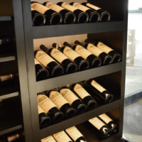Do you notice how the bottles fit perfectly into the shelves? This is because we custom-designed the wooden shelves according to the collection and the available space inside this glass wine room.